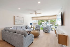A modern living room with a grey sectional sofa, patterned armchairs, a round ottoman, and a ceiling fan. - Martinique South 306 (Holmes Beach)