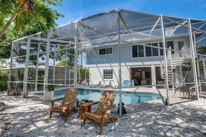 A covered outdoor area with a pool, wooden chairs, and a staircase leading to a deck. - Manatee Harbor (Anna Maria)