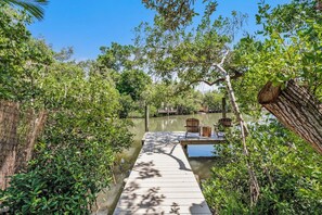 A wooden dock leading to a boat, surrounded by dense greenery and a calm body of water. - Manatee Harbor (Anna Maria)
