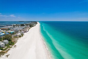 A coastal area with a long stretch of white sandy beach and clear turquoise waters. - Canal Front, Manatee Harbor by SeaBreeze Vacation (Anna Maria)