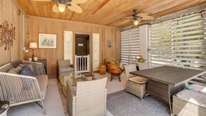 A room with wooden walls, ceiling fans, wicker furniture, a glass table, and a view through white blinds. - Canal Front, Manatee Harbor by SeaBreeze Vacation (Anna Maria)