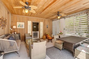 A room with wooden walls, ceiling fans, wicker furniture, a glass table, and a view through white blinds. - Canal Front, Manatee Harbor by SeaBreeze Vacation (Anna Maria)