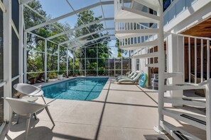 Un espace piscine extérieur doté d’une partie couverte, de chaises longues et offrant une vue sur un bâtiment avec balcon.