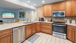A modern kitchen with wooden cabinets, stainless steel appliances, and a tiled backsplash. - Canal Front, Manatee Harbor by SeaBreeze Vacation (Anna Maria)