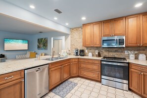 A modern kitchen with wooden cabinets, stainless steel appliances, and a tiled backsplash. - Canal Front, Manatee Harbor by SeaBreeze Vacation (Anna Maria)