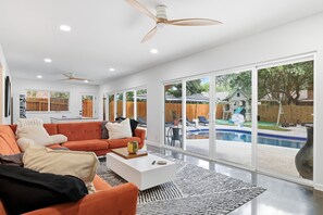 Ein modernes Wohnzimmer mit einem großen orangefarbenen Sofa, einem weißen Couchtisch und Blick auf einen Garten mit Pool.