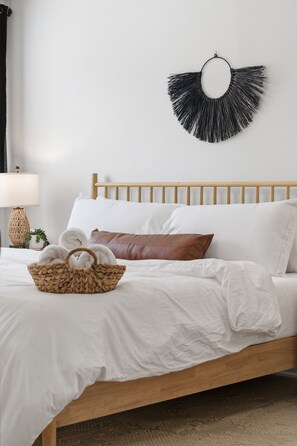 Ein Bett mit weißer Bettwäsche, einem Holzkopfende, einem gewebten Korb mit Handtüchern und einer schwarzen, runden Wanddekoration.