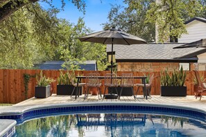 Ein Schwimmbecken mit Holzterrasse, Gartenmöbeln und Topfpflanzen.