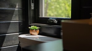 Een uitzicht op groen, een kleine plant in een pot op de vensterbank, en een wit toilet.