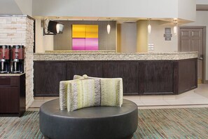 A modern hotel lobby with a bar area, a seating area with a patterned ottoman, and a large colorful artwork on the wall. - Residence Inn Detroit Livonia | 2 Studio Queen Rooms | Complimentary Breakfast (Livonia)