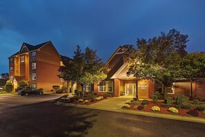 A hotel with a brick facade, multiple windows, and a well-maintained garden with various shrubs and flowers. - Residence Inn Detroit Livonia | 2 Studio Queen Rooms | Complimentary Breakfast (Livonia)
