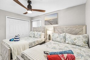 A bedroom with two beds, a ceiling fan, a window with blinds, a nightstand with a lamp, and a beach-themed wall art. - Waterfront Gulf Access Retreat with Heated Pool, Dock & Outdoor Fun - Villa Snowscape - Roelens (Cape Coral)