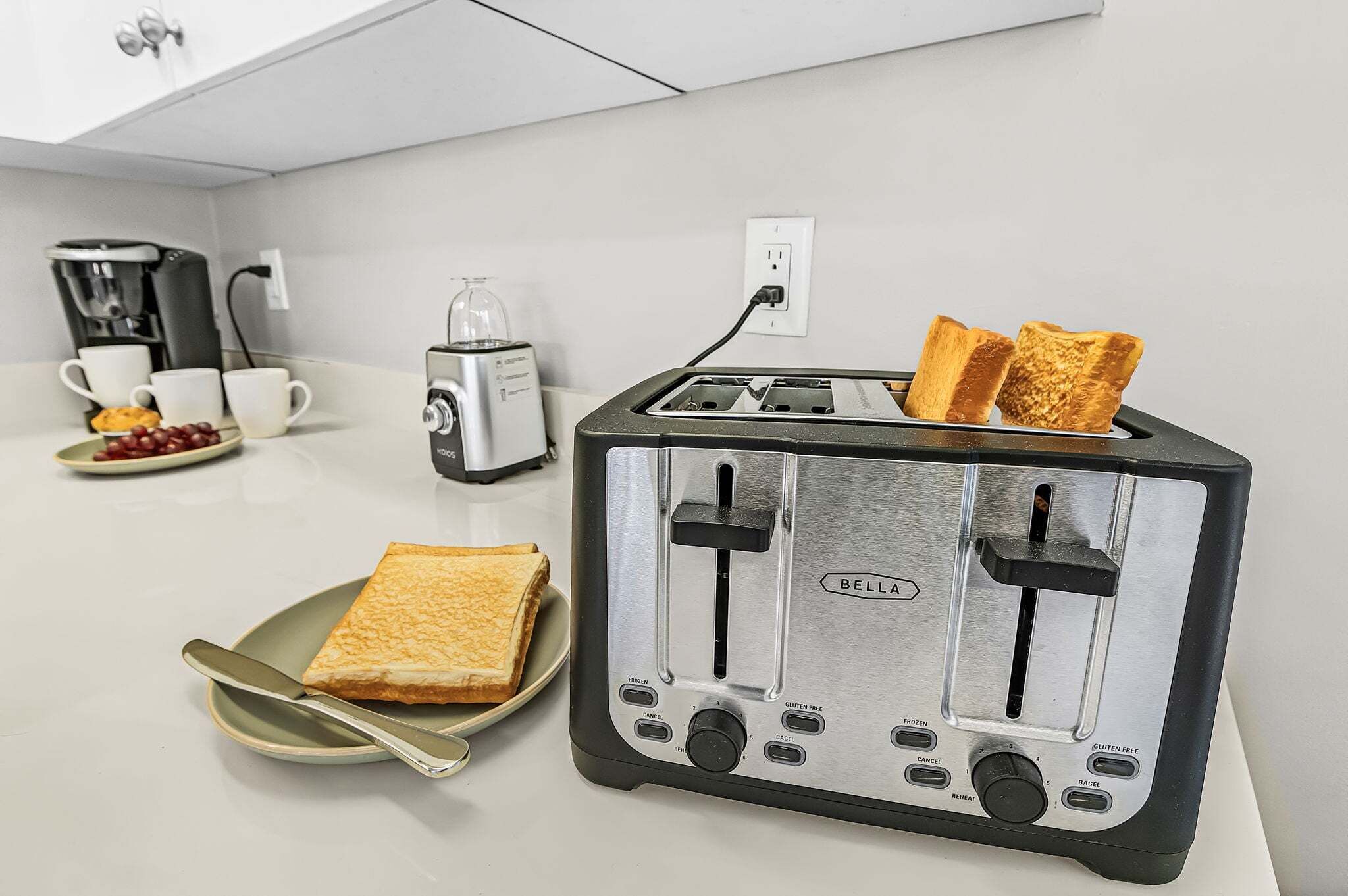 A kitchen with a toaster, a coffee maker, and a plate with toast and grapes.