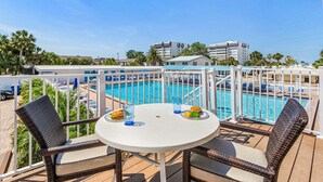 A balcony with a pool, wicker chairs, and a table with food and drinks. - Plunge into Fun & Sun at Siesta Key- A Coastal Gem - Aloha Kai Suite - Roelens (Sarasota)