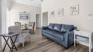 A living room with a leather sofa, a dining area with wicker chairs, and a ceiling fan. - Plunge into Fun & Sun at Siesta Key- A Coastal Gem - Aloha Kai Suite - Roelens (Sarasota)