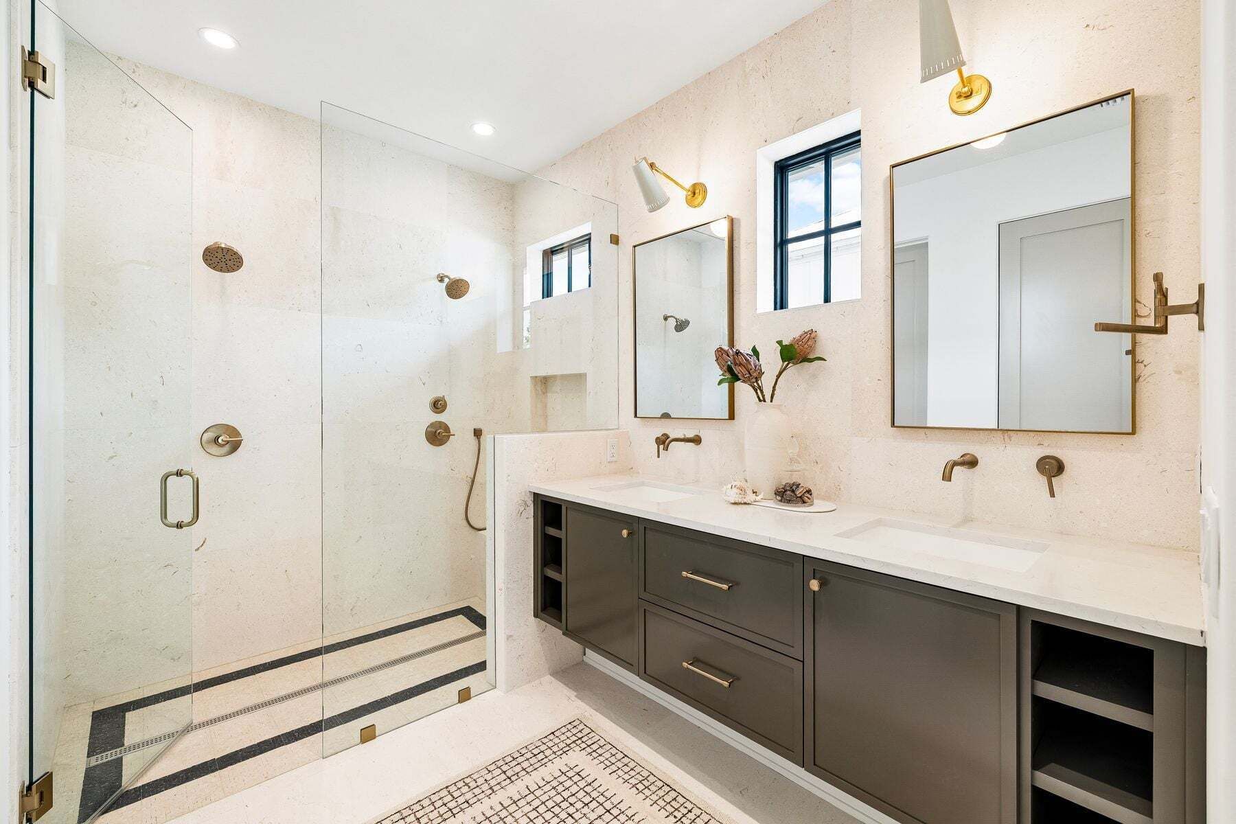 A modern bathroom with a glass shower enclosure, a vanity with a large mirror, and a sink with a vase of dried flowers.