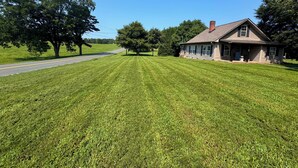 A house with a well-maintained lawn, a road in the background, and trees around.