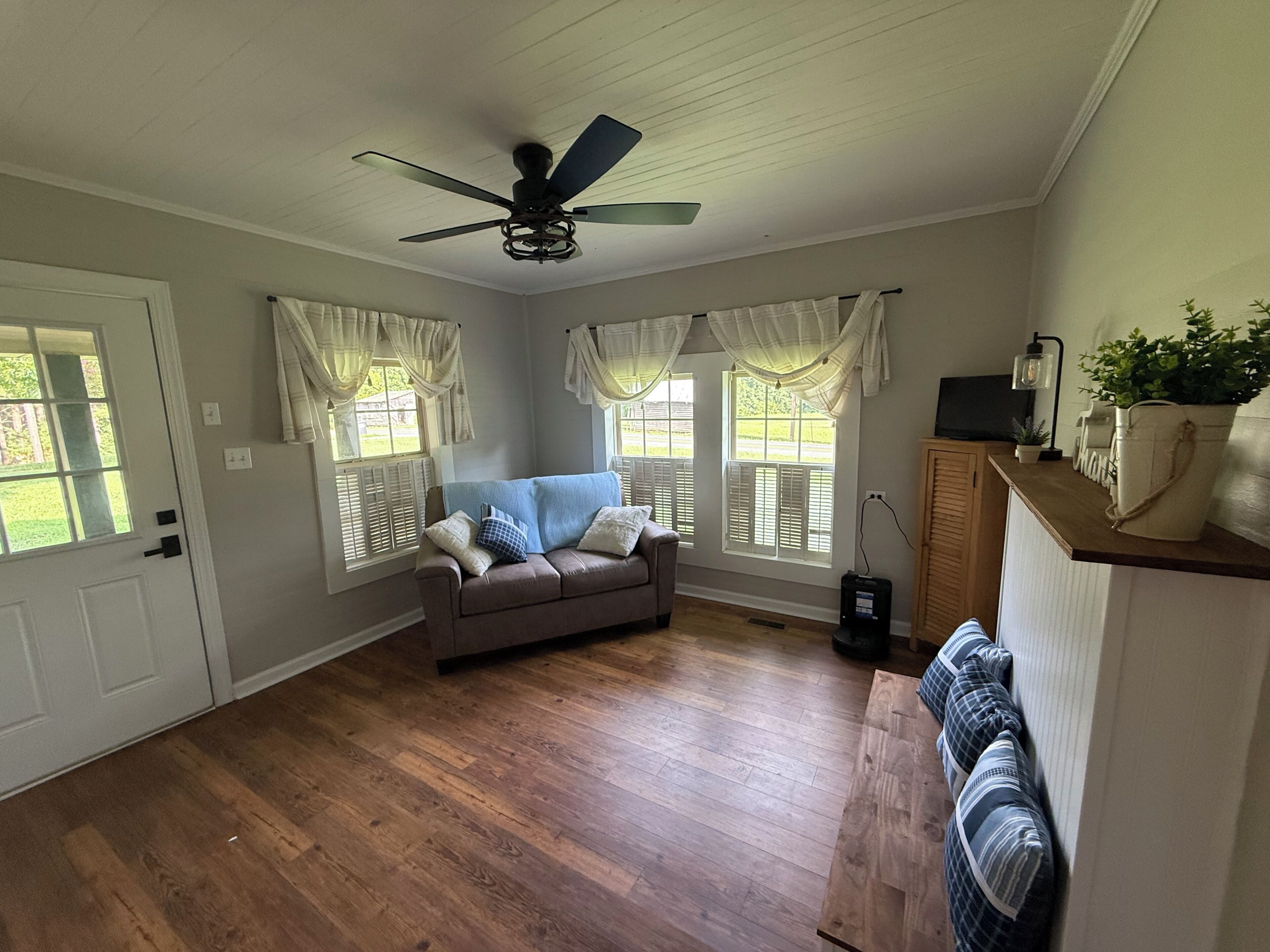 A room with a ceiling fan, a brown leather sofa, and a wooden floor.