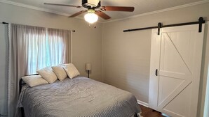 A bedroom with a bed, a ceiling fan, a window with curtains, and a door.
