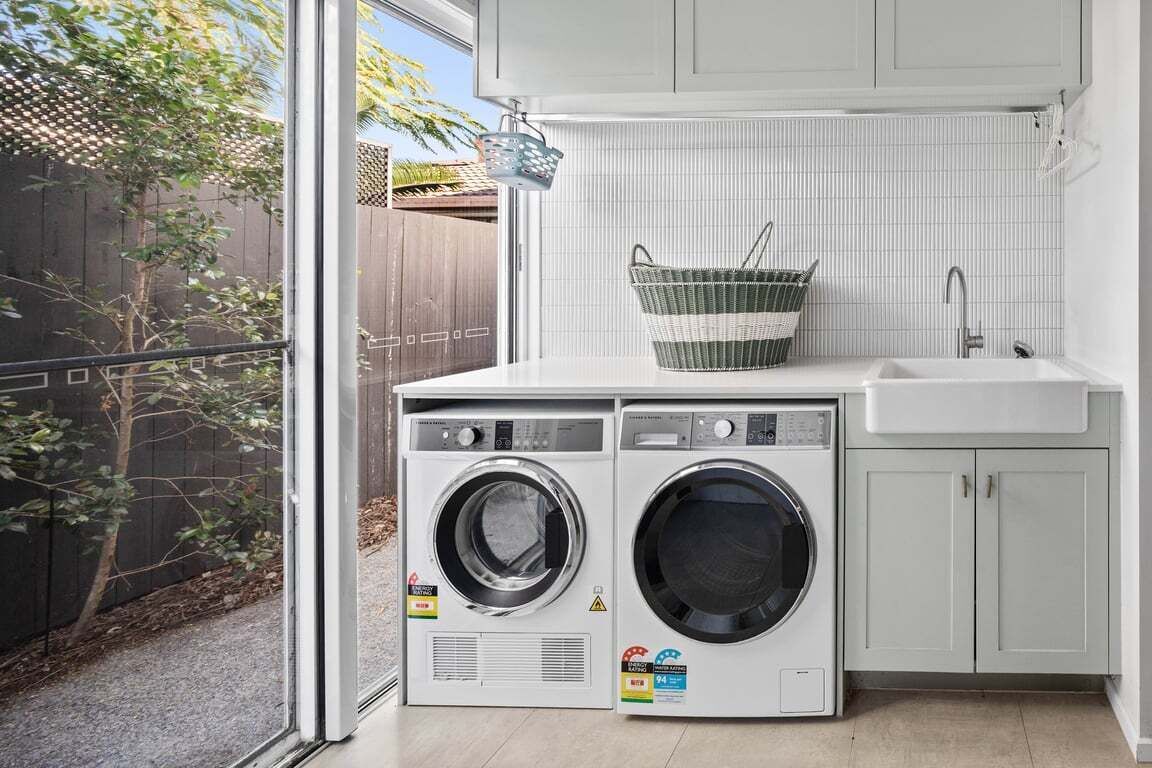 A laundry area with two front-loading washing machines, a sink, and a basket.