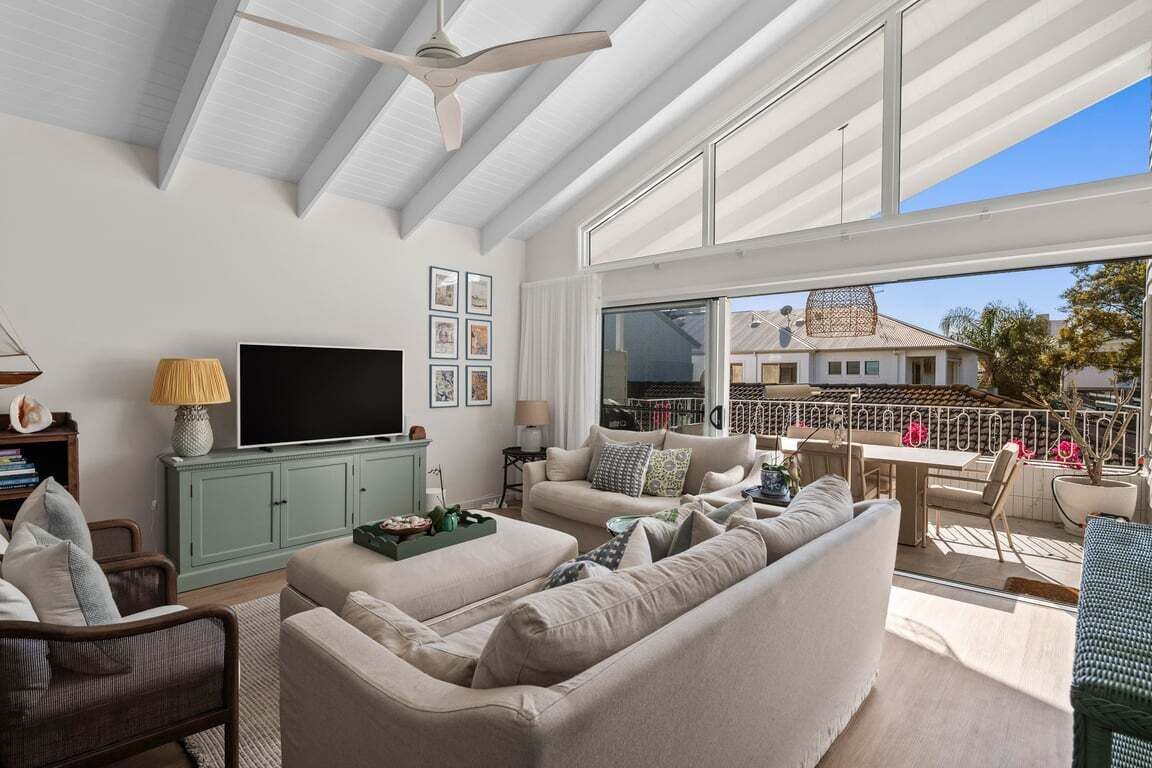 A spacious living room with a flat-screen TV, comfortable seating, and a balcony with a view of the neighborhood.