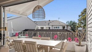 Eine Terrasse im Freien mit Tisch und Stühlen, einer hängenden Leuchte und Blick auf ein Gebäude im Hintergrund.