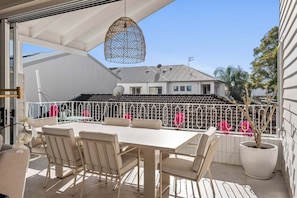 An outdoor patio with a table and chairs, a hanging light fixture, and a view of a building in the background. - Curly’s Beach House (Gold Coast)