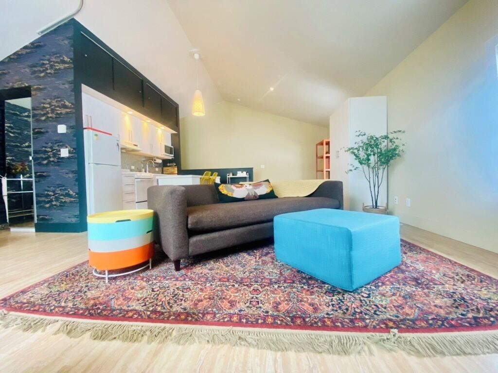 A modern living room with a sofa, ottoman, and colorful rug.