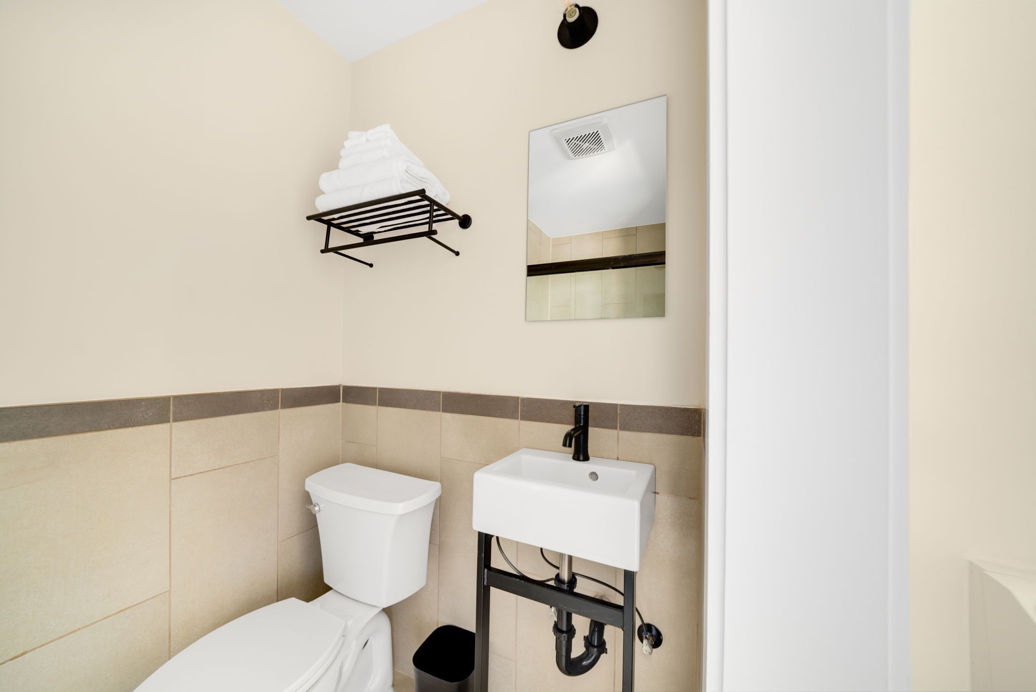 Un baño con inodoro, lavamanos, toallero y espejo.