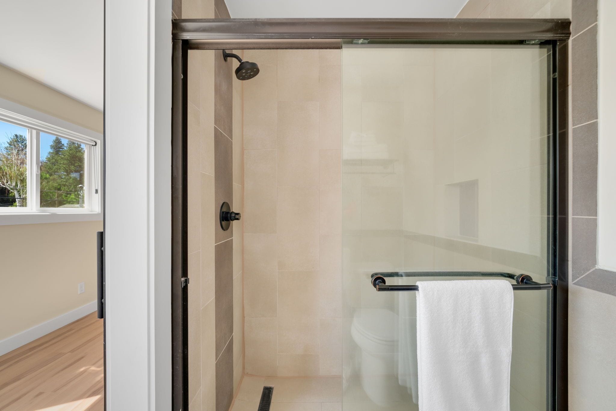 A glass-enclosed shower with a glass door, a towel rack with a towel, and a window with a view of trees.