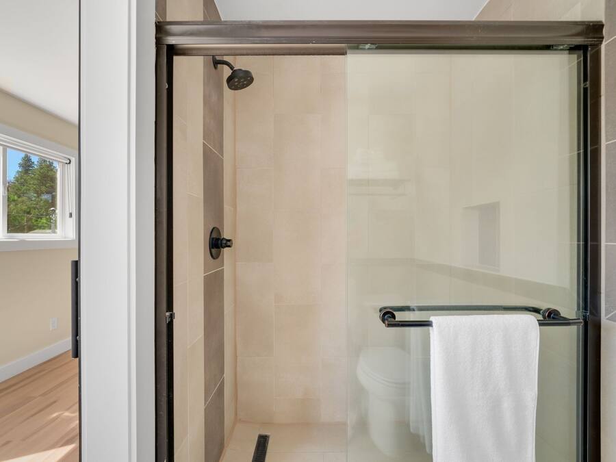 A glass-enclosed shower with a glass door, a towel rack with a towel, and a window with a view of trees.
