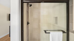Ducha con paredes de vidrio, un perchero y una toalla blanca.