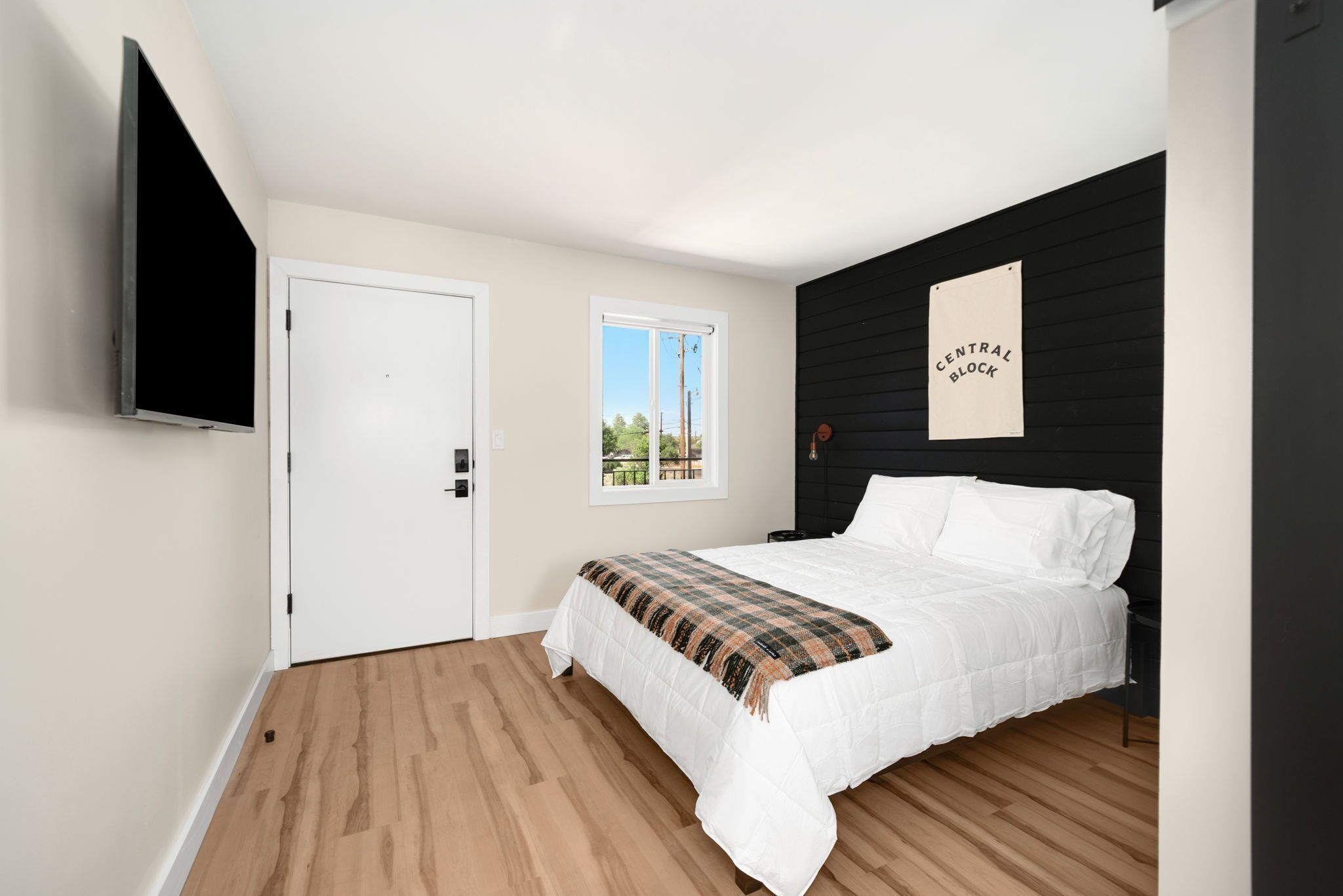 A bedroom with a bed, a TV mounted on the wall, a window, and a door.