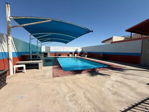 Ein Swimmingpool mit blauem Sonnensegel, einem weißen Stuhl und einem Tisch.