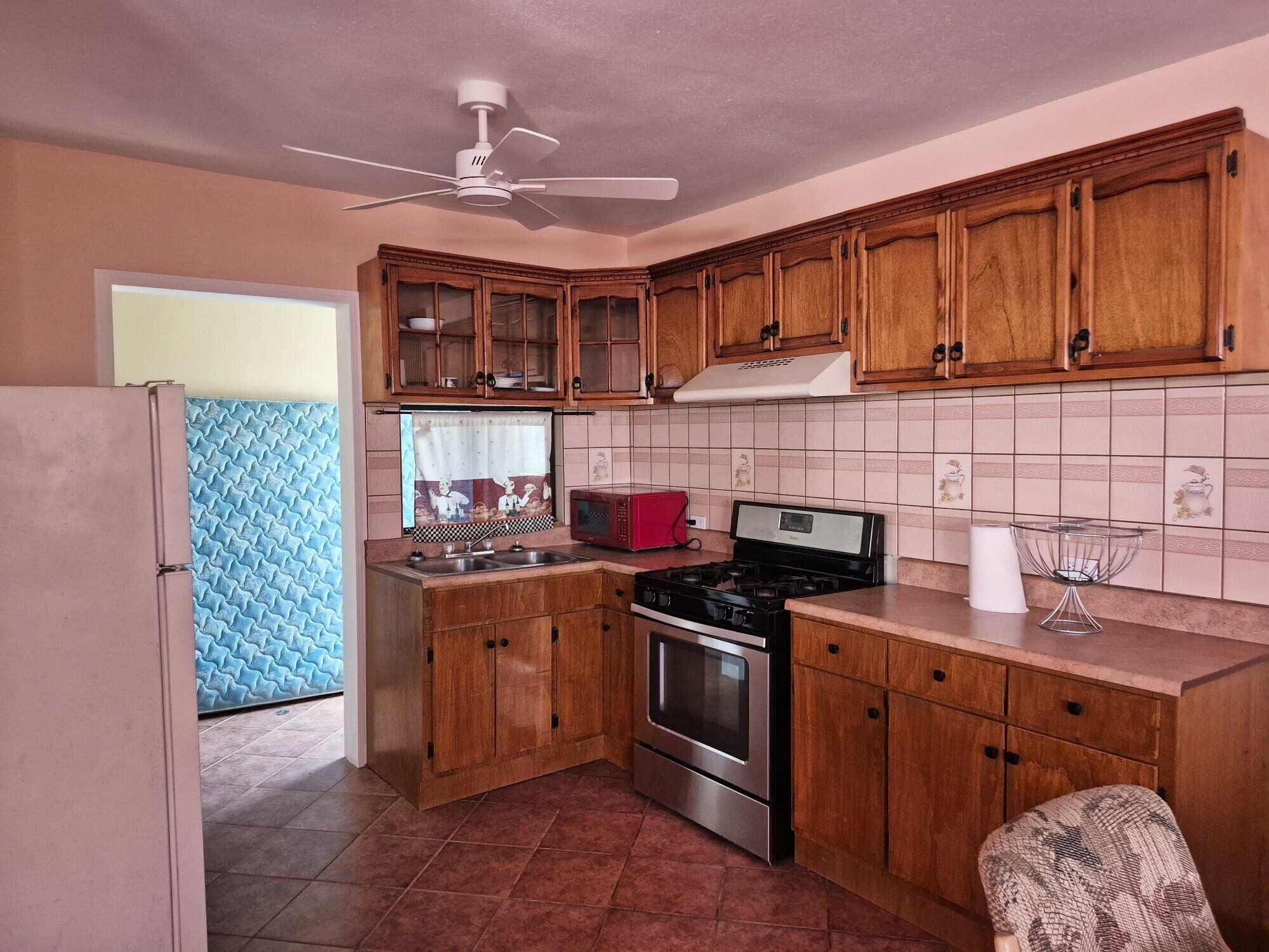 An interior perspective of the spacious kitchen layout, showcasing classic wooden cabinets, expansive countertops, a stainless steel gas oven range, and a full-size refrigerator.