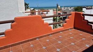 Uma varanda com guarda-corpos laranja, soalho de azulejos e vista para o mar e edifícios.