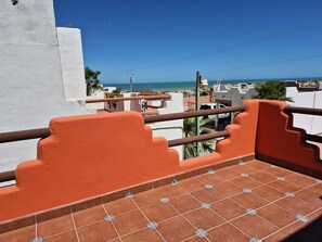 Ein Balkon mit orangefarbenen Geländern, einem Kachelboden und Blick auf Meer und Gebäude.