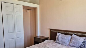 Quarto com cama, guarda-roupa, mesa de cabeceira, ventoinha no teto e aparelho de ar condicionado.