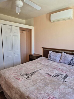 Ein Schlafzimmer mit Bett, Kleiderschrank, Nachttisch, Deckenventilator und Klimaanlage.