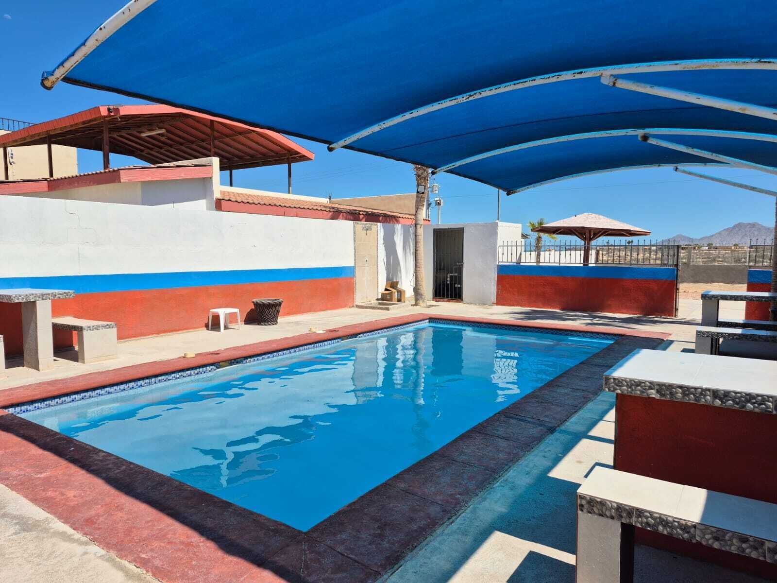 A final look across the calm waters of the communal swimming pool, highlighting the extensive blue canopy overhead and the open, sunny concrete deck space surrounding the facility.