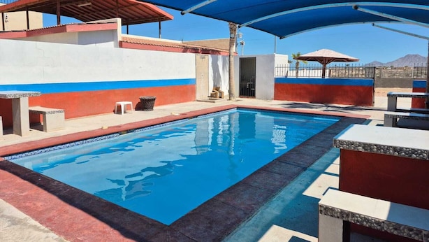 En swimmingpool med blå og hvide farver, omgivet af udendørs siddepladser og skyggefulde områder.