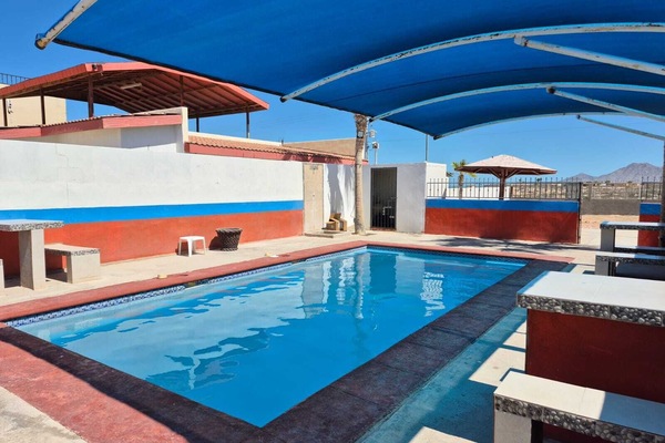 A final look across the calm waters of the communal swimming pool, highlighting the extensive blue canopy overhead and the open, sunny concrete deck space surrounding the facility.