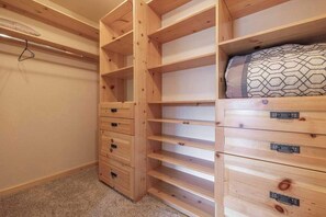 A wooden storage unit with multiple drawers and shelves, a hanging garment rack, and a bed with a patterned pillow. - Golden Oak Estate | 7BR Luxury. Wine Room. Views. (Big Bear Lake)
