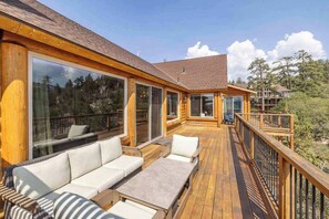 A wooden deck with outdoor seating and large windows. - Golden Oak Estate | 7BR Luxury. Wine Room. Views. (Big Bear Lake)