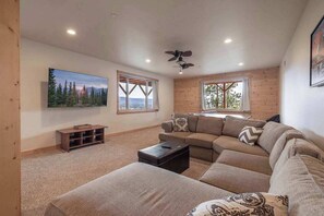 A modern living room with a sectional sofa, a flat-screen TV, and a ceiling fan. - Golden Oak Estate | 7BR Luxury. Wine Room. Views. (Big Bear Lake)