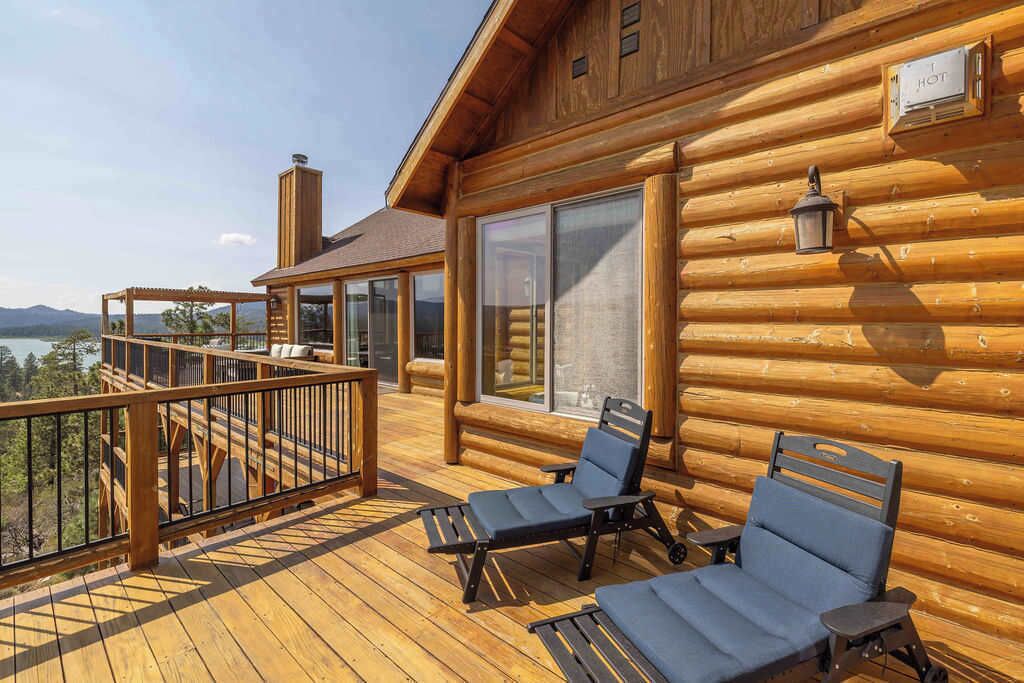 Eine Holzhütte mit einer Terrasse, zwei Liegestühlen und Blick auf die Berge.