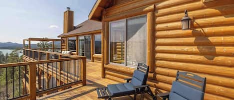 Una cabaña de madera con terraza, dos sillones de descanso y vistas a la montaña.