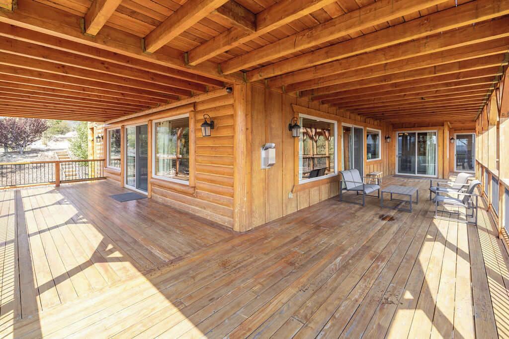 Eine Holzterrasse mit überdachtem Bereich, großen Fenstern und Gartenmöbeln.