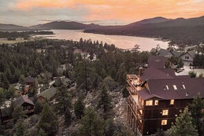 A residential area with multiple houses surrounded by dense forest, a lake, and mountains in the background. - Golden Oak Estate | 7BR Luxury. Wine Room. Views. (Big Bear Lake)