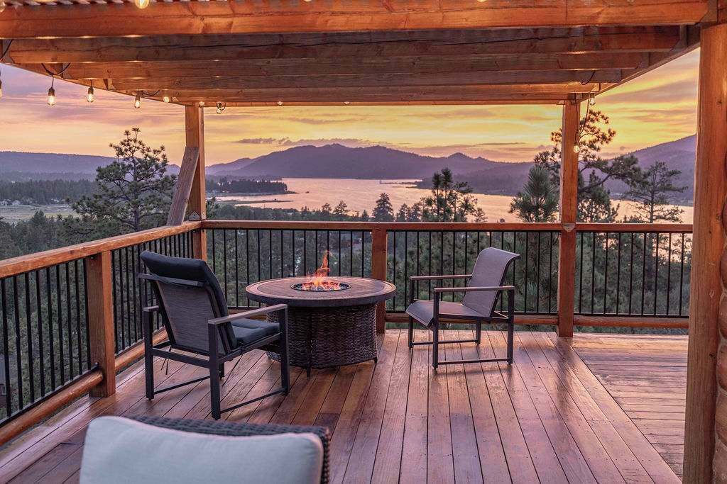 Eine Holzterrasse mit Feuerstelle und zwei Stühlen mit Blick auf einen See und Berge.